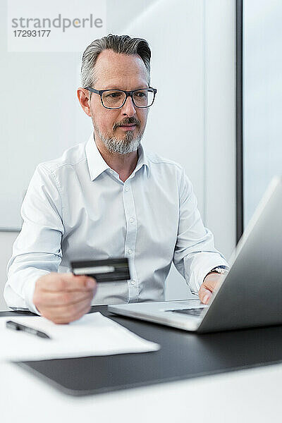 Männlicher Unternehmer mit Kreditkarte und Laptop im Büro