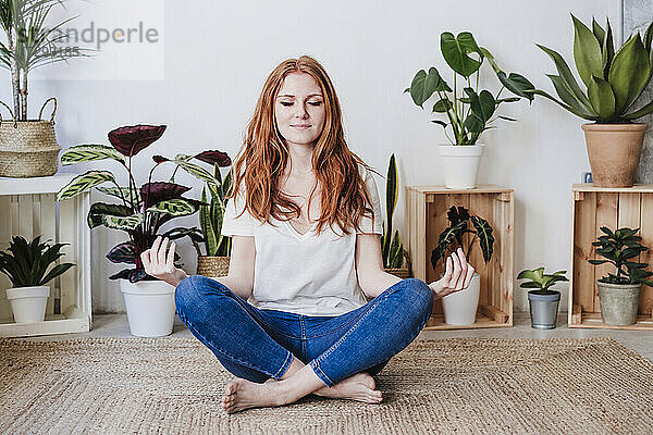 Rothaarige Frau meditiert  während sie zu Hause auf dem Boden sitzt