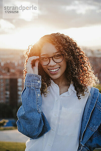 Junge Frau  die bei Sonnenuntergang eine Brille berührt