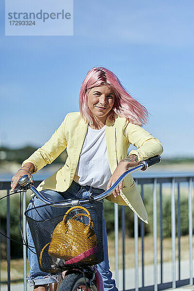 Lächelnde Frau mit Fahrrad am Geländer an einem sonnigen Tag
