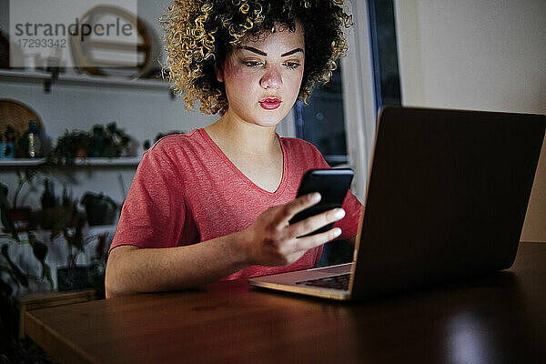 Schöne junge Frau sitzt mit Laptop und benutzt ein Smartphone zu Hause