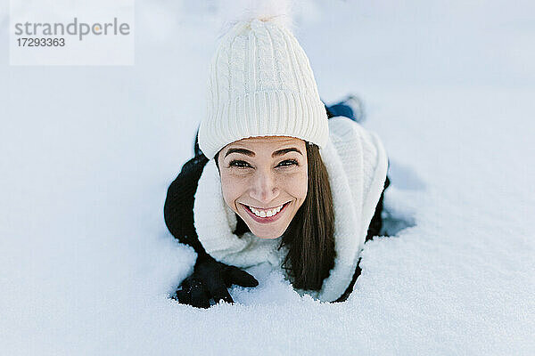 Glückliche Frau mit Strickmütze auf Schnee liegend