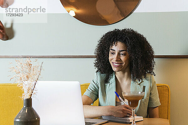 Lächelnde Geschäftsfrau  die im Restaurant am Laptop in ein Buch schreibt