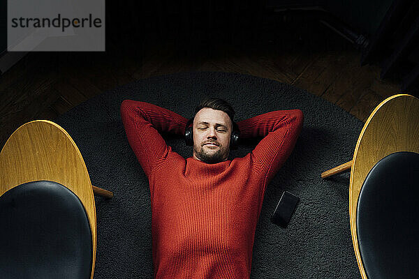 Entspannter Geschäftsmann mit Kopfhörern auf dem Teppich liegend am Arbeitsplatz