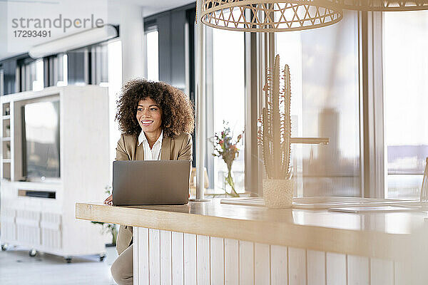 Lächelnde Geschäftsfrau  die vor einem Laptop in einer Büro-Cafeteria steht und nachdenkt