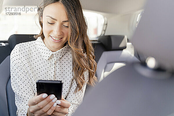 Lächelnde Unternehmerin  die ein Smartphone benutzt  während sie im Auto sitzt