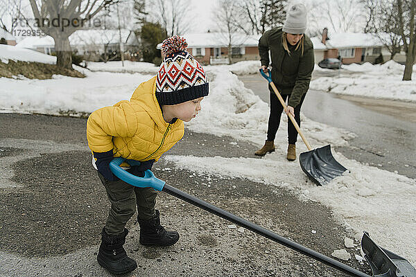 Sohn hilft Mutter beim Schneeschaufeln in der Einfahrt