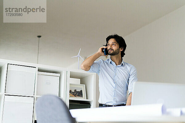 Männlicher Unternehmer  der im Büro mit einem Mobiltelefon spricht