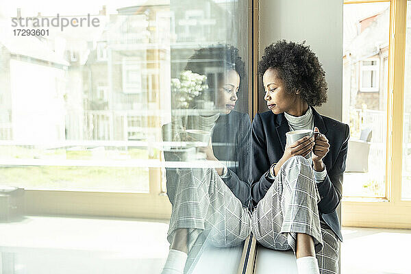 Weibliche Fachkraft schaut nach unten  während sie auf der Fensterbank im Büro sitzt