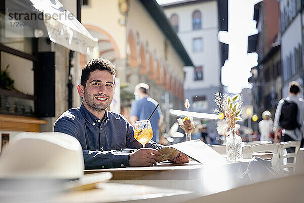 Männlicher Tourist mit Getränk und Karte in einem Straßencafé an einem sonnigen Tag