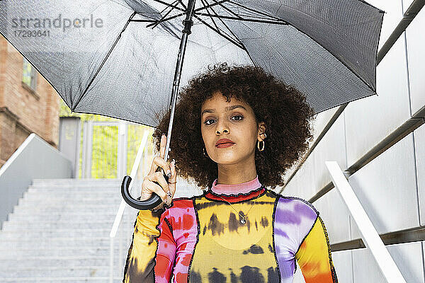 Junge Frau mit lockigem Haar  die einen Regenschirm hält und starrt