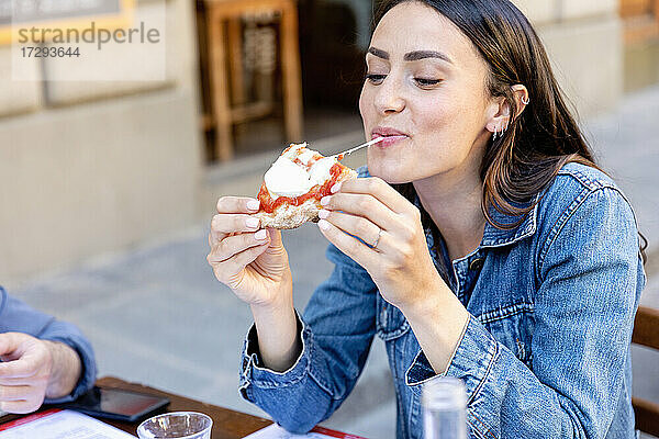 Lächelnde Frau isst Pizza in einem Straßencafé