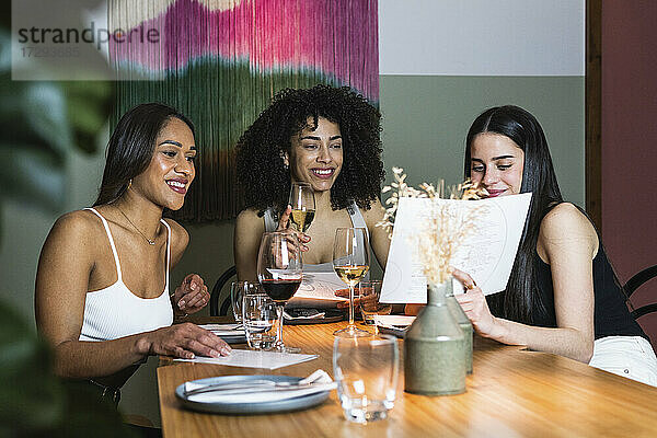Frau zeigt Freunden die Speisekarte  während sie in einem Restaurant etwas trinkt