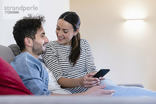 Lächelndes Paar mit Smartphone auf dem Sofa zu Hause