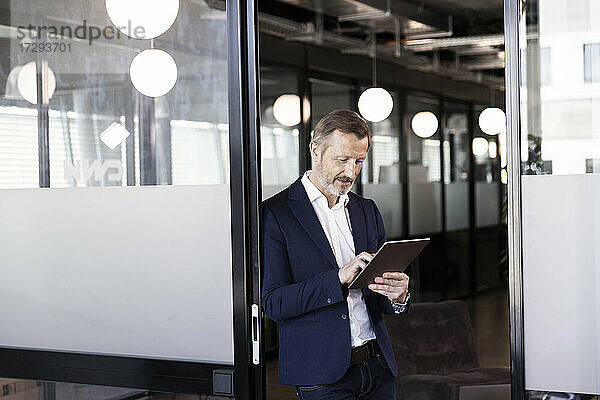 Geschäftsmann arbeitet an einem digitalen Tablet an einer Glastür im Büro