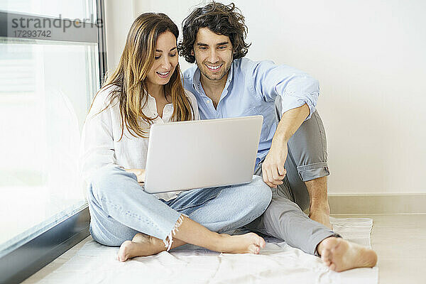 Lächelnde Freundin und Freund benutzen gemeinsam einen Laptop zu Hause