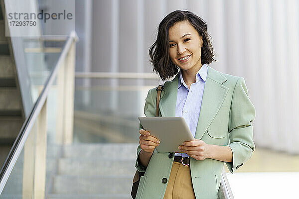 Lächelnde weibliche Fachkraft mit digitalem Tablet in einem Bürogebäude
