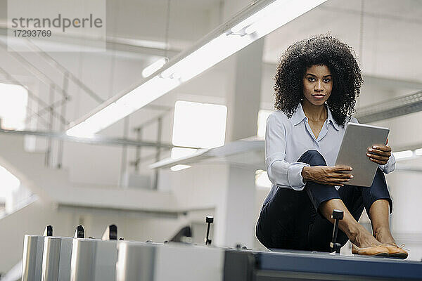 Geschäftsfrau mit digitalem Tablet an einer Maschine in der Industrie sitzend