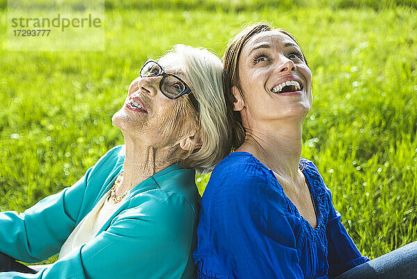Glückliche ältere Frau und Frau im mittleren Erwachsenenalter blicken auf  während sie in einem öffentlichen Park sitzen