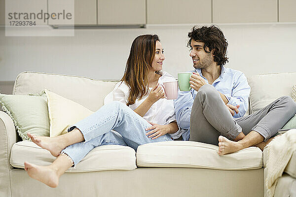 Lächelndes Paar beim Kaffee auf dem Sofa im neuen Haus