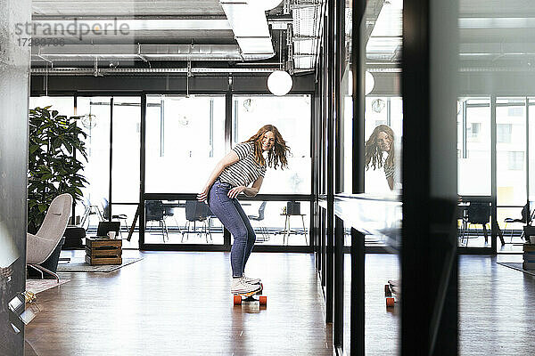 Lächelnde weibliche Fachkraft beim Skateboardfahren im Büro