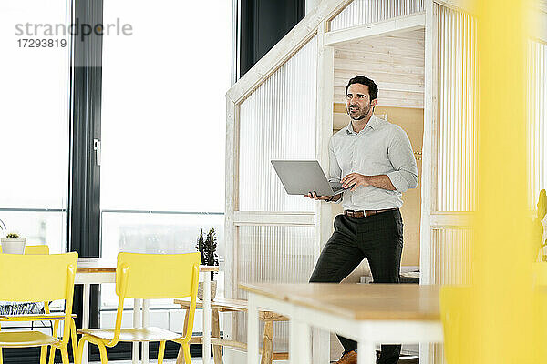 Männlicher Unternehmer  der seinen Blick abwendet  während er in der Cafeteria einen Laptop in der Hand hält