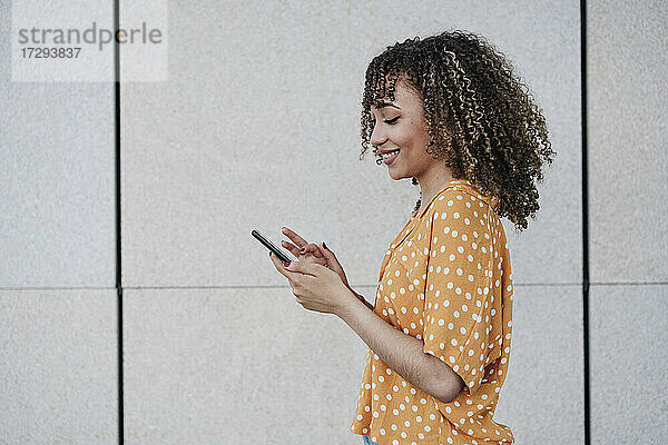 Junge Frau benutzt Smartphone an der Wand