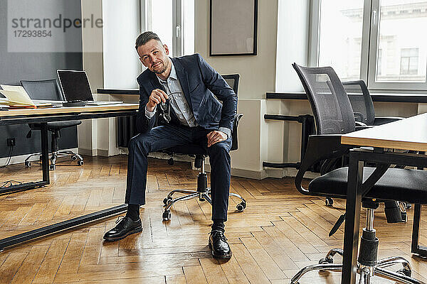 Selbstbewusster Geschäftsmann sitzt auf einem Stuhl im Büro