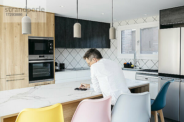 Geschäftsmann  der ein Mobiltelefon benutzt  während er zu Hause an der Kücheninsel sitzt