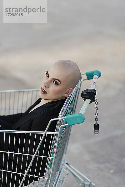 Glatzköpfige Transgender-Frau im Einkaufswagen sitzend