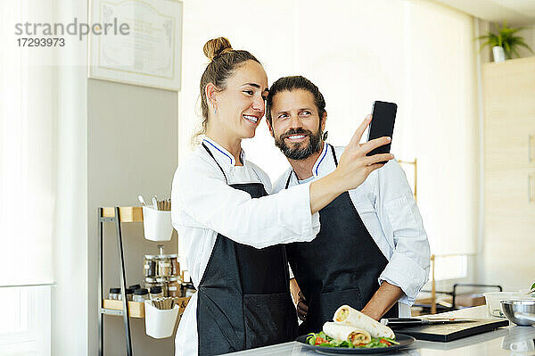 Glückliche Köche machen ein Selfie mit ihrem Handy in der Küche eines modernen Restaurants