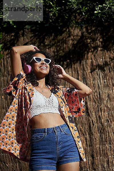 Lächelnde Frau hört Musik über Kopfhörer beim Tanzen an einem sonnigen Tag