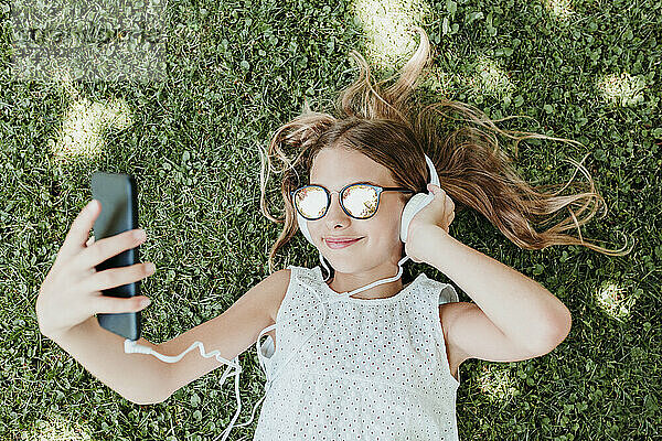 Lächelndes Mädchen  das ein Handy benutzt  während es im Gras liegt