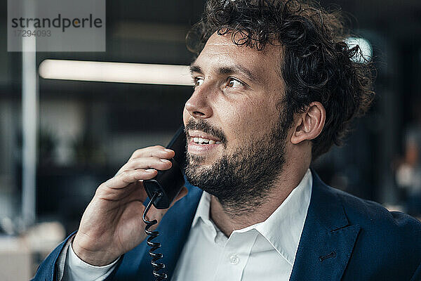 Männlicher Unternehmer schaut weg  während er im Büro telefoniert