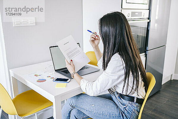 Junge Freiberuflerin liest ein Dokument  während sie zu Hause im Büro sitzt