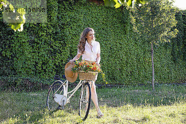 Junge Frau  die bei einem sonnigen Spaziergang im Garten ein Fahrrad schiebt