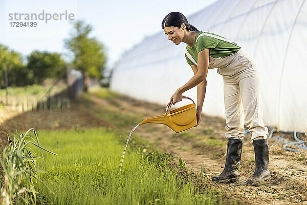 Junge Bäuerin beim Bewässern von Pflanzen auf einem Biohof