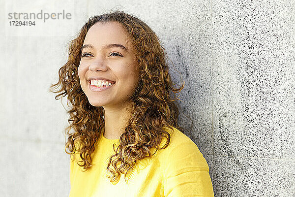 Lächelnde junge Frau träumt vor einer Wand