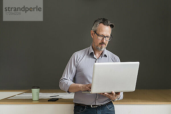 Männlicher Unternehmer  der im Stehen im Büro einen Laptop benutzt