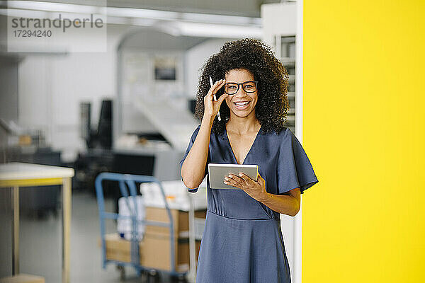 Lächelnde Geschäftsfrau mit digitalem Tablet  die eine Brille im Büro einstellt