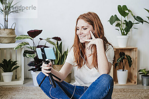 Schöne Frau lächelnd während Videoanruf durch Smartphone auf dem Boden zu Hause