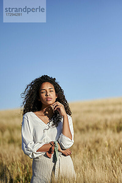 Nachdenkliche junge Frau mit lockigem Haar in einem Weizenfeld stehend