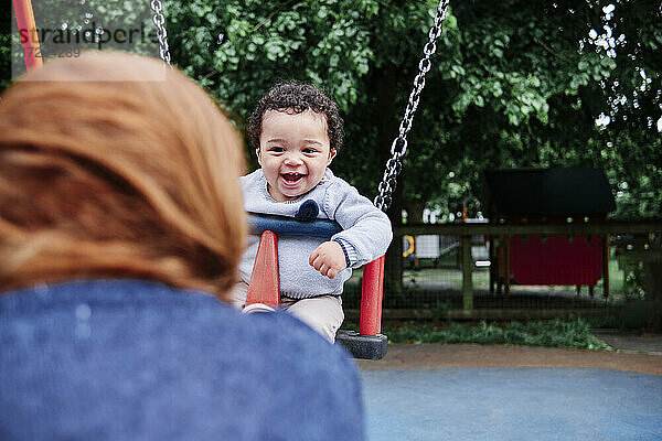 Lächelnder Junge beim Schaukeln auf dem Spielplatz im Park