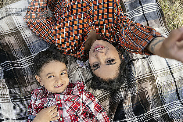 Lächelnde Mutter  die ein Selfie mit ihrem Sohn macht  während sie auf einer Picknick-Decke liegt