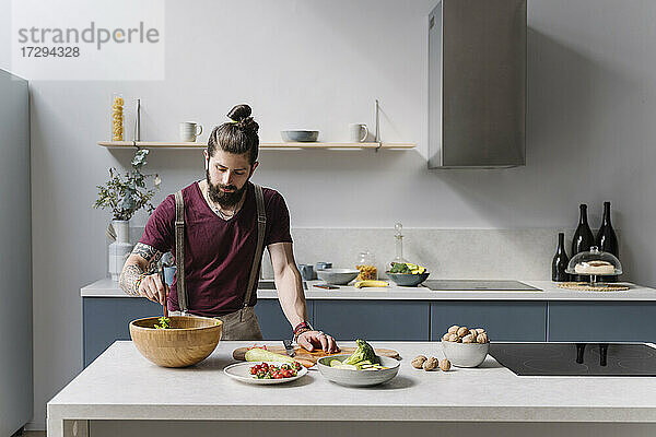 Mittlerer erwachsener Mann bereitet Salat zu  während er an einer Kücheninsel steht