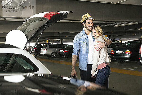 Lächelnder Mann umarmt Freundin auf dem Flughafenparkplatz