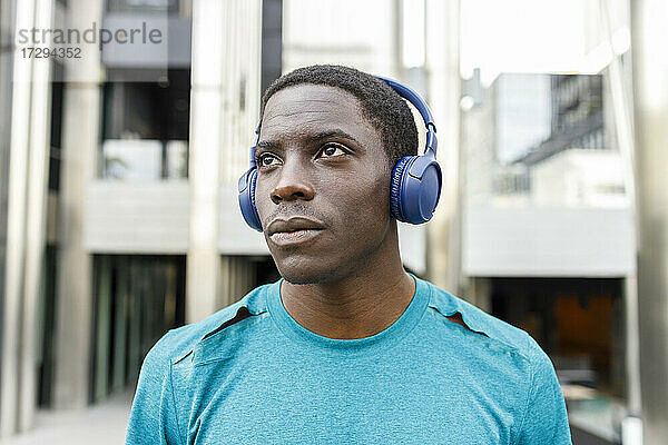 Afro-Mann  der nachdenklich ist  während er über Kopfhörer am Gebäudeeingang Musik hört