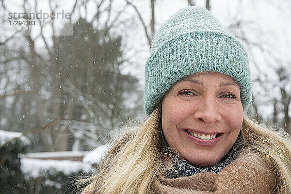 Lächelnde schöne blonde Frau mit Strickmütze im Schnee