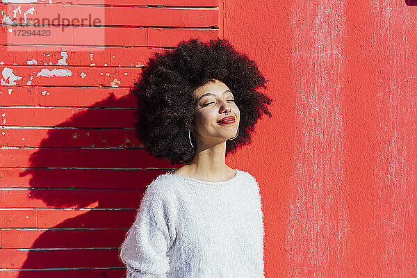 Afro Haar Frau lächelnd vor roter Wand stehend