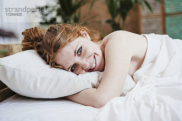 Lächelnde Frau mit Decke auf dem Bett liegend zu Hause